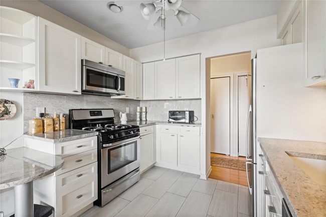 Kitchen featuring appliances with stainless steel finishes, white cabinetry, tasteful backsplash, ceiling fan, and light stone counters | Image 10