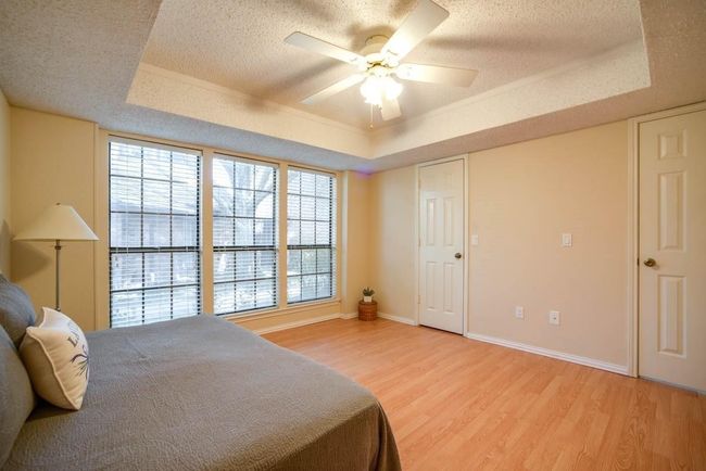 Bedroom featuring a raised ceiling, light wood-style floors, baseboards, a textured ceiling, and ceiling fan | Image 13