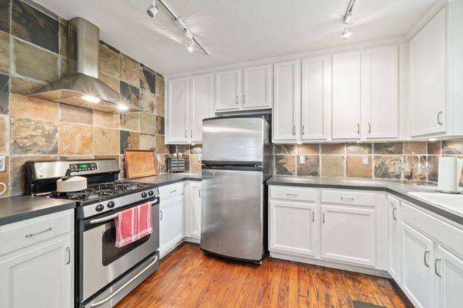 Kitchen featuring stainless steel appliances, track lighting, wall chimney range hood, white cabinets, and backsplash | Image 5