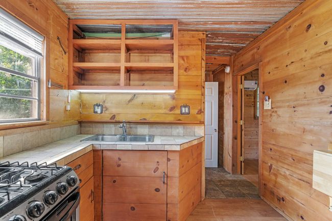 Kitchen with a sink, tile countertops, open shelves, wooden walls, and brown cabinets | Image 18