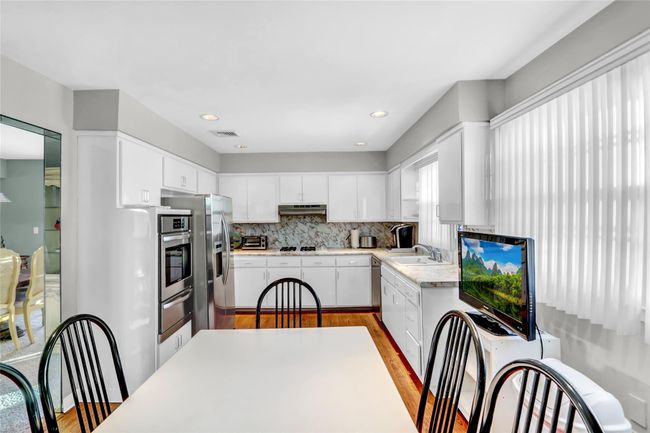 Kitchen with sink, appliances with stainless steel finishes, white cabinetry, tasteful backsplash, and light wood-type flooring | Image 13