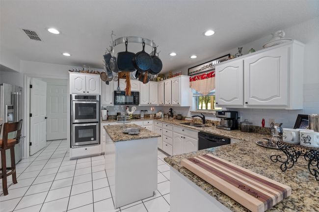 Kitchen featuring visible vents, a center island, white cabinets, a sink, and black appliances | Image 10