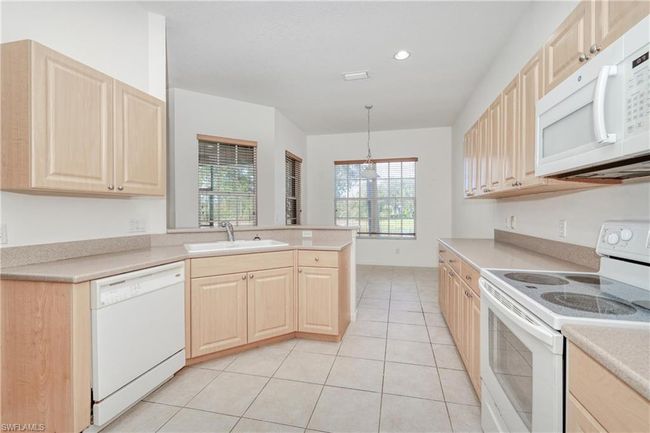 Kitchen with a wealth of natural light, pendant lighting, light brown cabinetry, sink, and white appliances | Image 26