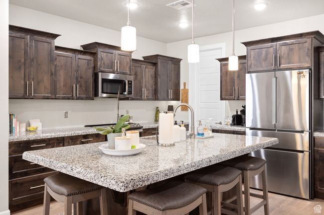Kitchen with appliances with stainless steel finishes, a kitchen breakfast bar, dark brown cabinets, light wood finished floors, and an island with sink | Image 48