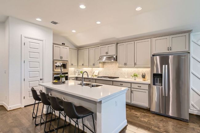 Kitchen with stainless steel appliances, under cabinet range hood, dark wood-type flooring, vaulted ceiling, and tasteful backsplash | Image 10
