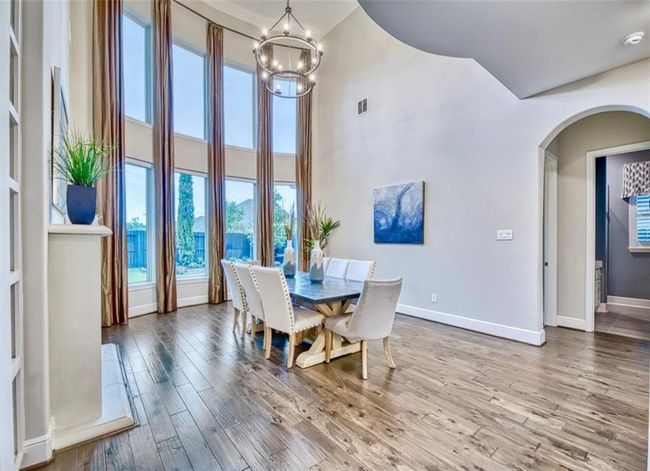 This spacious dining area features high ceilings and large windows that provide ample natural light. It includes elegant wood flooring, a modern chandelier, and a stylish dining set, creating a welcoming and sophisticated ambiance. | Image 11