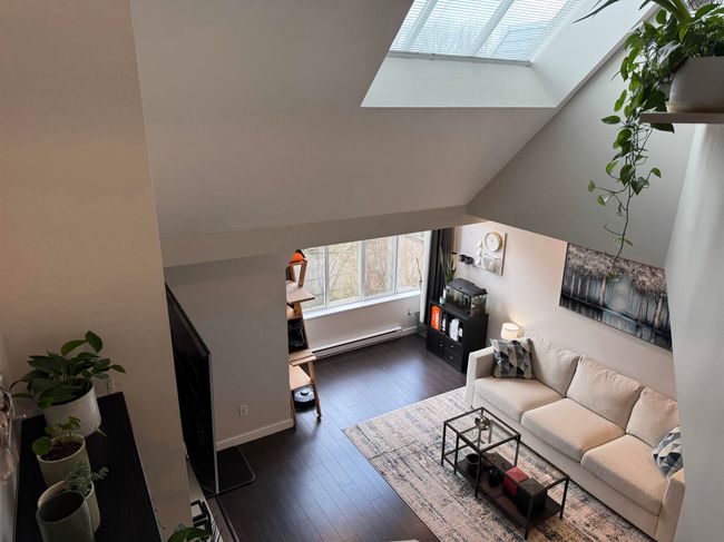Living room with vaulted ceiling with skylight, baseboard heating, and dark wood-style flooring | Image 12