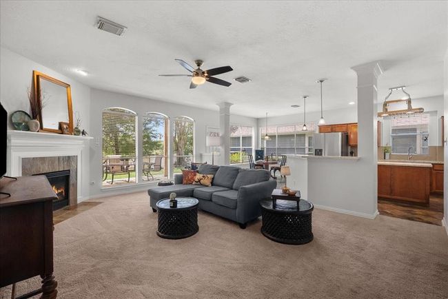 Bright, open-concept living area with a cozy fireplace and large windows while connecting seamlessly to the kitchen with a breakfast bar. | Image 7