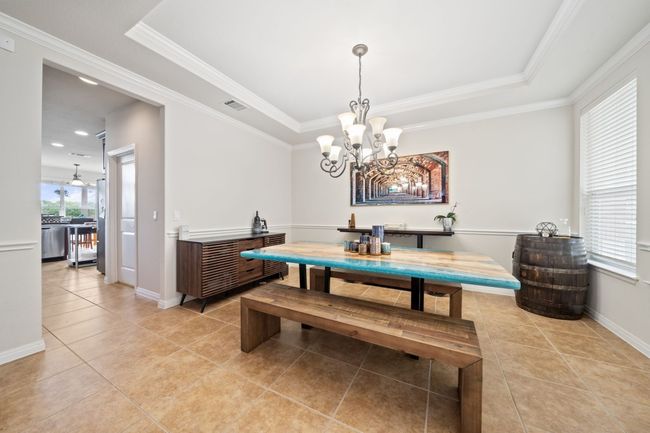 Dining room featuring a chandelier, a tray ceiling, light tile patterned floors, and crown molding | Image 7