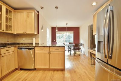 Kitchen featuring decorative light fixtures, stainless steel appliances, light brown cabinets and hardwood flooring | Image 2