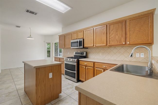 Kitchen with decorative backsplash, a kitchen island, visible vents, appliances with stainless steel finishes, and a sink | Image 15