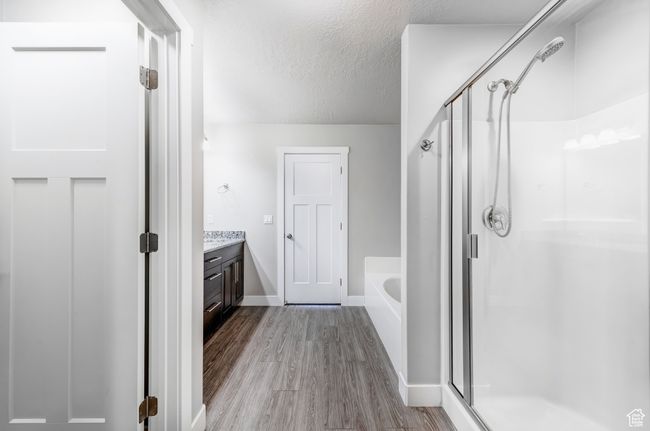 Bathroom with a bath, a stall shower, a soaking tub, a textured ceiling, and wood finished floors | Image 12