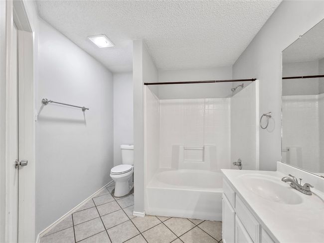 Bathroom with toilet, vanity, tile patterned floors, bathtub / shower combination, and a textured ceiling | Image 4