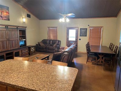 Living room with a barn door, ceiling fan, wooden ceiling, lofted ceiling, and crown molding | Image 2