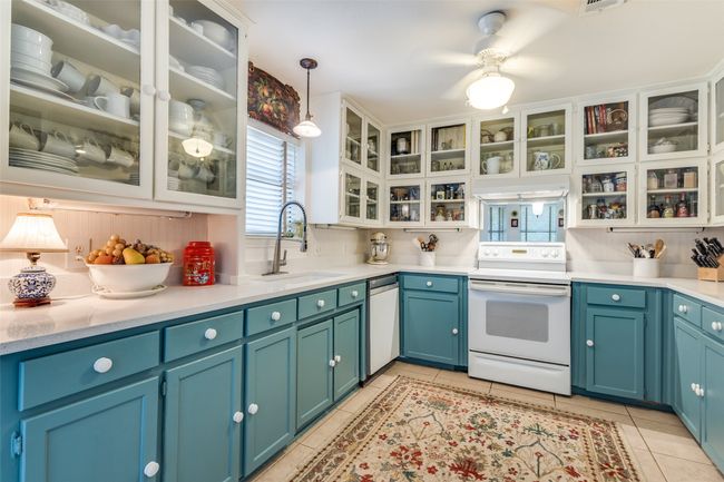 Kitchen with white appliances, a sink, light tile patterned floors, light countertops, and glass insert cabinets | Image 14
