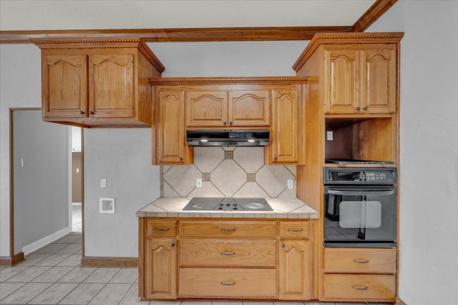 Kitchen featuring black appliances, range hood, decorative backsplash, tile countertops, and light tile patterned flooring | Image 12
