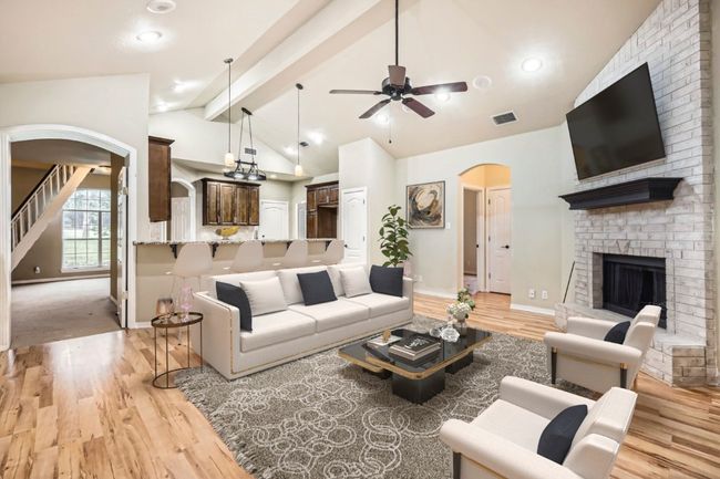 Living area with arched walkways, a ceiling fan, light wood finished floors, a brick fireplace, and beam ceiling | Image 5