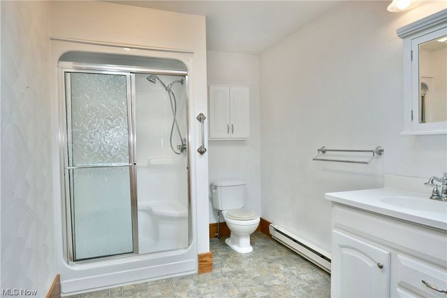 Bathroom featuring large vanity, tile flooring, toilet, baseboard heating, and a shower with door | Image 20