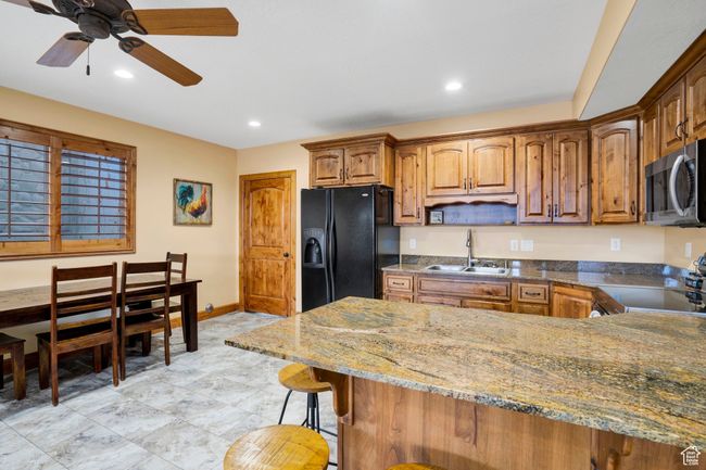 Kitchen featuring black fridge with ice dispenser, stove, stainless steel microwave, a sink, and ceiling fan | Image 34