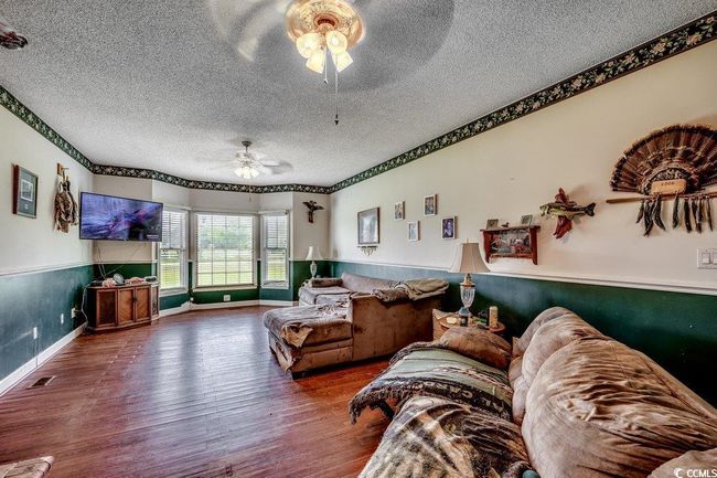 Living room with a ceiling fan, a textured ceiling, wood finished floors, baseboards, and a wainscoted wall | Image 9