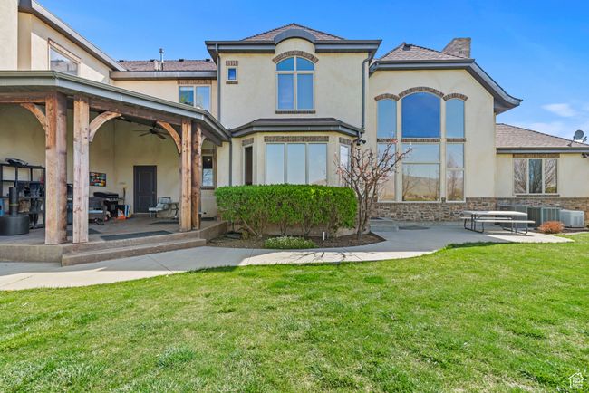 Rear view of property with a ceiling fan, stone siding, a lawn, a patio, and stucco siding | Image 7