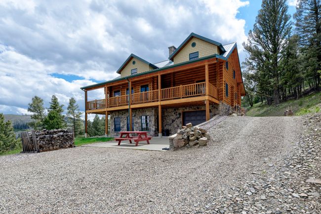 Rear view of property featuring stone siding, log siding, driveway, a chimney, and an attached garage | Image 56