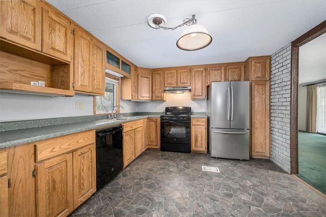 Kitchen with under cabinet range hood, open shelves, a sink, stone finish flooring, and black appliances | Image 16