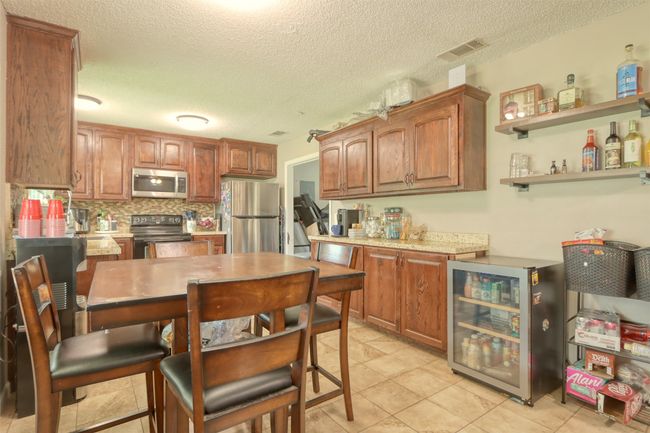 Kitchen featuring stainless steel appliances, wine cooler, decorative backsplash, a textured ceiling, and light countertops | Image 15