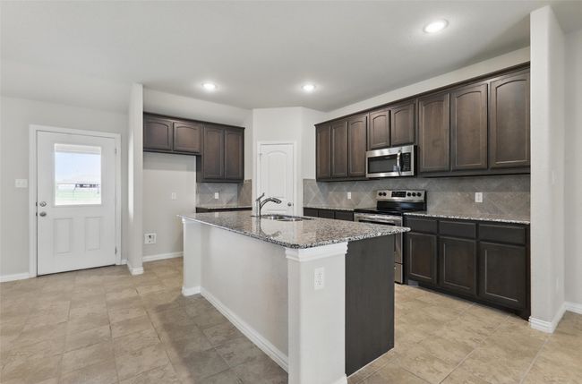 Kitchen featuring stainless steel appliances, a sink, light stone countertops, dark brown cabinets, and decorative backsplash | Image 10