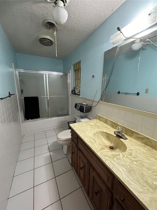 Full bath featuring toilet, tile patterned flooring, a textured ceiling, vanity, and tile walls | Image 14
