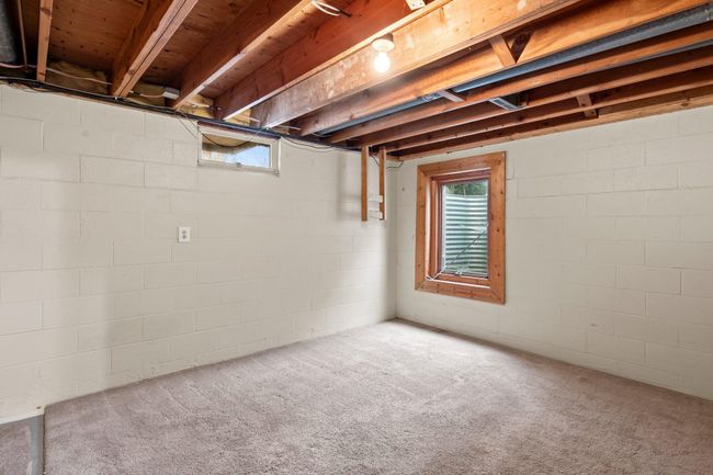 An alternate view of the unfinished basement showcases a carpeted area with an egress window, allowing natural light to brighten the space. | Image 13