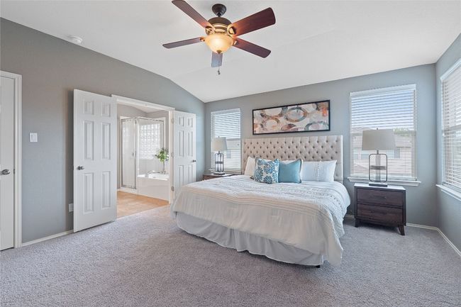 Carpeted bedroom with lofted ceiling, multiple windows, ensuite bathroom, and a ceiling fan | Image 26