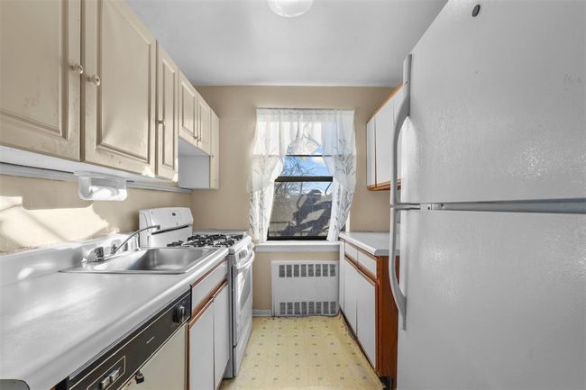 Kitchen featuring white appliances, light flooring, radiator heating unit, and light countertops | Image 4