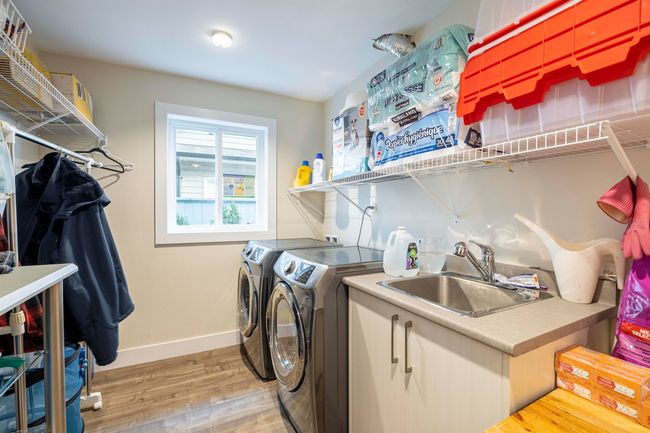 Clothes washing area with baseboards, light wood finished floors, washing machine and clothes dryer, laundry area, and a sink | Image 19