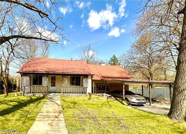 View of front of property featuring a tile roof, a chimney, covered porch, an attached carport, and a front yard | Image 43