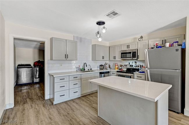 Kitchen with stainless steel appliances, separate washer and dryer, backsplash, light wood-style floors, and pendant lighting | Image 13