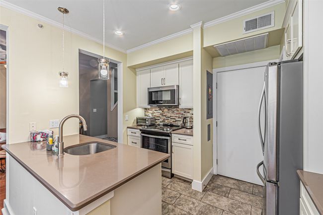 Kitchen featuring appliances with stainless steel finishes, decorative backsplash, a peninsula, white cabinetry, and crown molding | Image 12