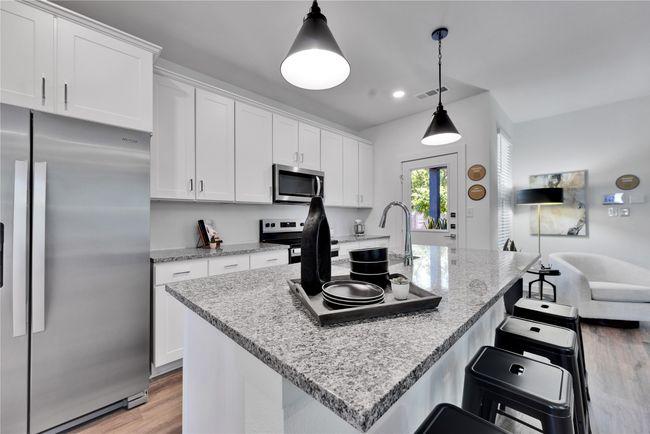 Kitchen with stainless steel appliances, visible vents, white cabinets, and light wood-style flooring | Image 11