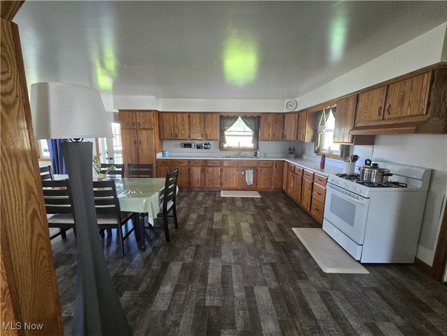 Kitchen with brown cabinetry, light countertops, gas range gas stove, and dark wood-style flooring | Image 4