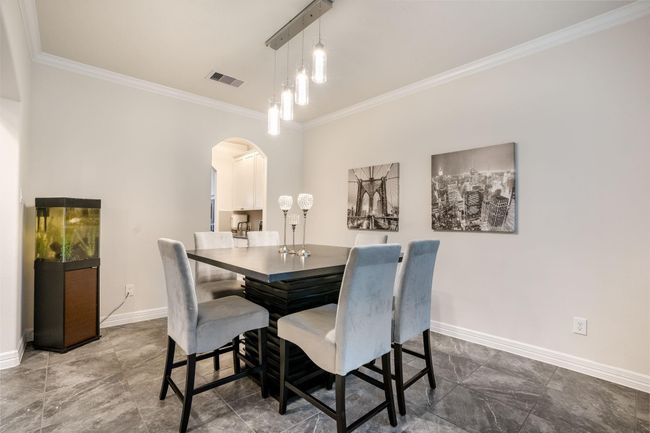 This dining area features a modern setup with a contemporary pendant lighting, an open archway leading to the kitchen, all set on sleek tiled flooring. | Image 6