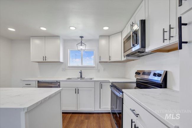 Kitchen featuring appliances with stainless steel finishes, white cabinetry, pendant lighting, dark wood-type flooring, and light stone counters | Image 7