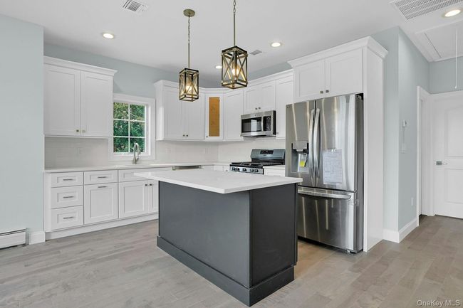 Kitchen featuring stainless steel appliances, white cabinets, light countertops, light wood-type flooring, and recessed lighting | Image 9