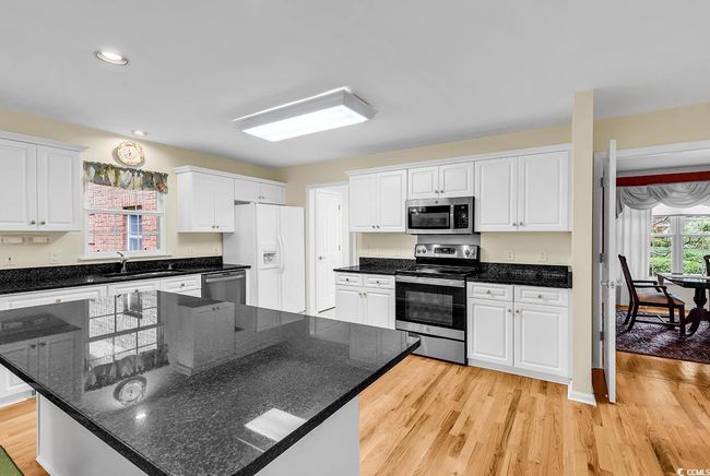 Kitchen with appliances with stainless steel finishes, white cabinetry, light wood-style flooring, a center island, and recessed lighting | Image 23