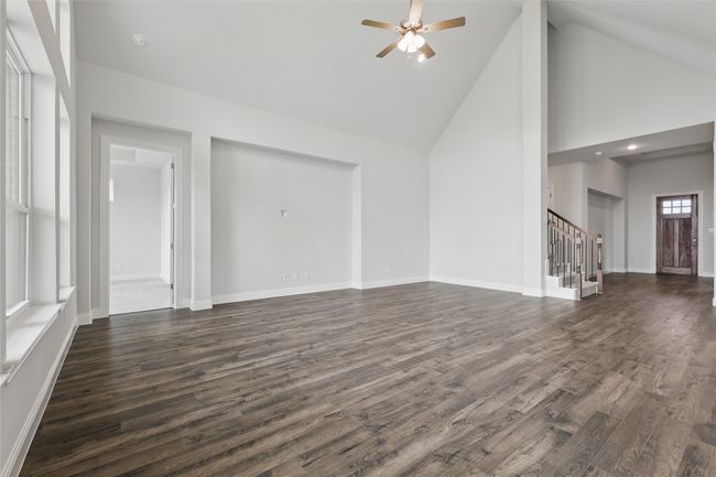 Unfurnished living room with stairway, high vaulted ceiling, baseboards, dark wood-type flooring, and ceiling fan | Image 10