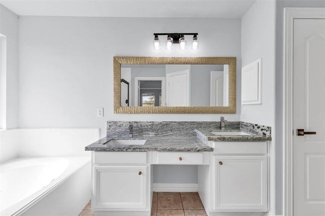 Modern bathroom with dual sinks and granite countertops. Features a large mirror, stylish lighting, and a soaking tub. Neutral colors create a serene atmosphere. | Image 29