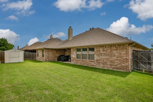 Rear view of property featuring a fenced backyard, a chimney, a shed, brick siding, and a shingled roof | Image 40