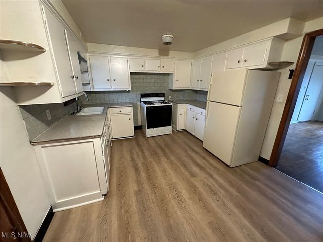 Kitchen featuring dark wood finished floors, white appliances, decorative backsplash, a sink, and white cabinetry | Image 4