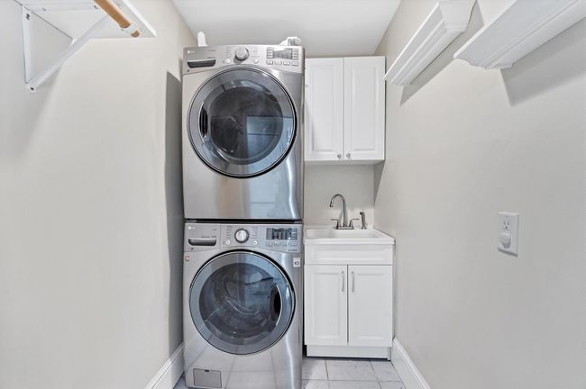 Laundry area featuring stacked washing machine and dryer, cabinet space, baseboards, and light marble finish flooring | Image 26