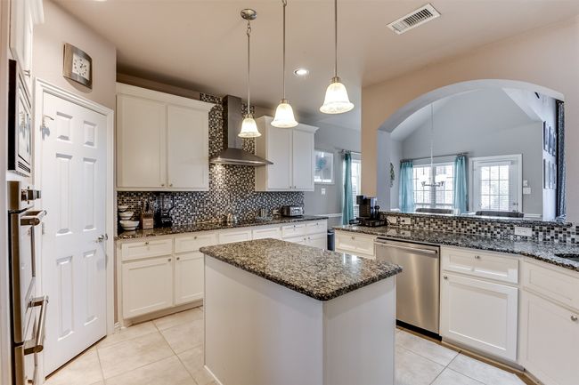 Kitchen featuring white cabinetry, a center island, wall chimney exhaust hood, hanging light fixtures, and stainless steel dishwasher | Image 18
