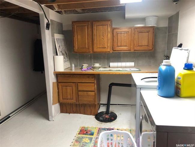 Kitchen featuring light countertops, brown cabinetry, decorative backsplash, an office area, and washer / dryer | Image 46